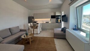 A modern living room with a sofa, coffee table, and a kitchen area in the background. - Aloft Suites Mykonos Island (Mykonos)