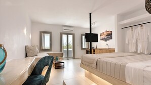 A modern bedroom with a bed, a desk, a chair, a TV, and a bathroom with a mirror and towel rack. - Aloft Suites Mykonos Island (Mykonos)