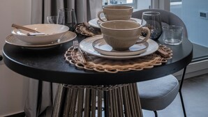 Una mesa de comedor con platos, tazones y vasos, frente a una ventana que ofrece vistas de edificios blancos y un cielo despejado.