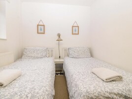 Un dormitorio con dos camas individuales, una mesita de noche con lámpara y dos cuadros en la pared.