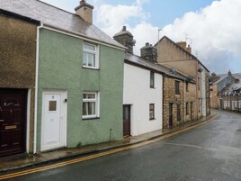 A narrow street lined with traditional buildings, featuring a mix of stone and painted facades, with a clear road and double yellow lines.