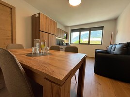 A modern kitchen with wooden cabinets, a dining table with chairs, and a view of mountains through a window.