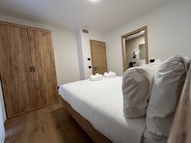 A bedroom with a large wooden wardrobe, a bed with white linens, and a mirror on the wall.