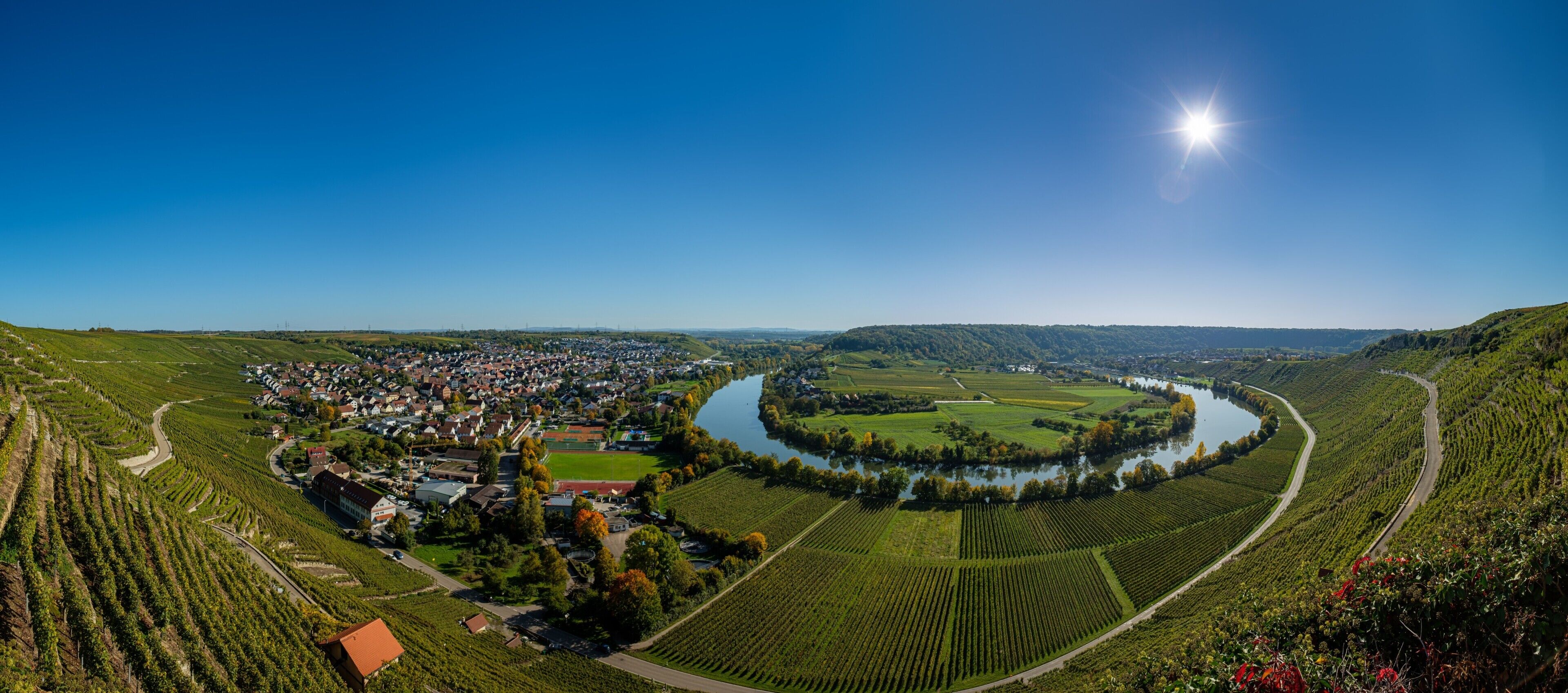 Une vue panoramique d’une ville avec une rivière, des vignobles et un ciel dégagé.