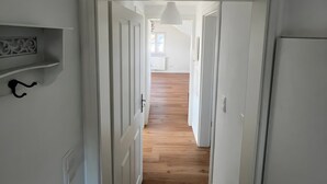 Un pasillo estrecho con puertas blancas y suelo de madera que conduce a una habitación con ventana.