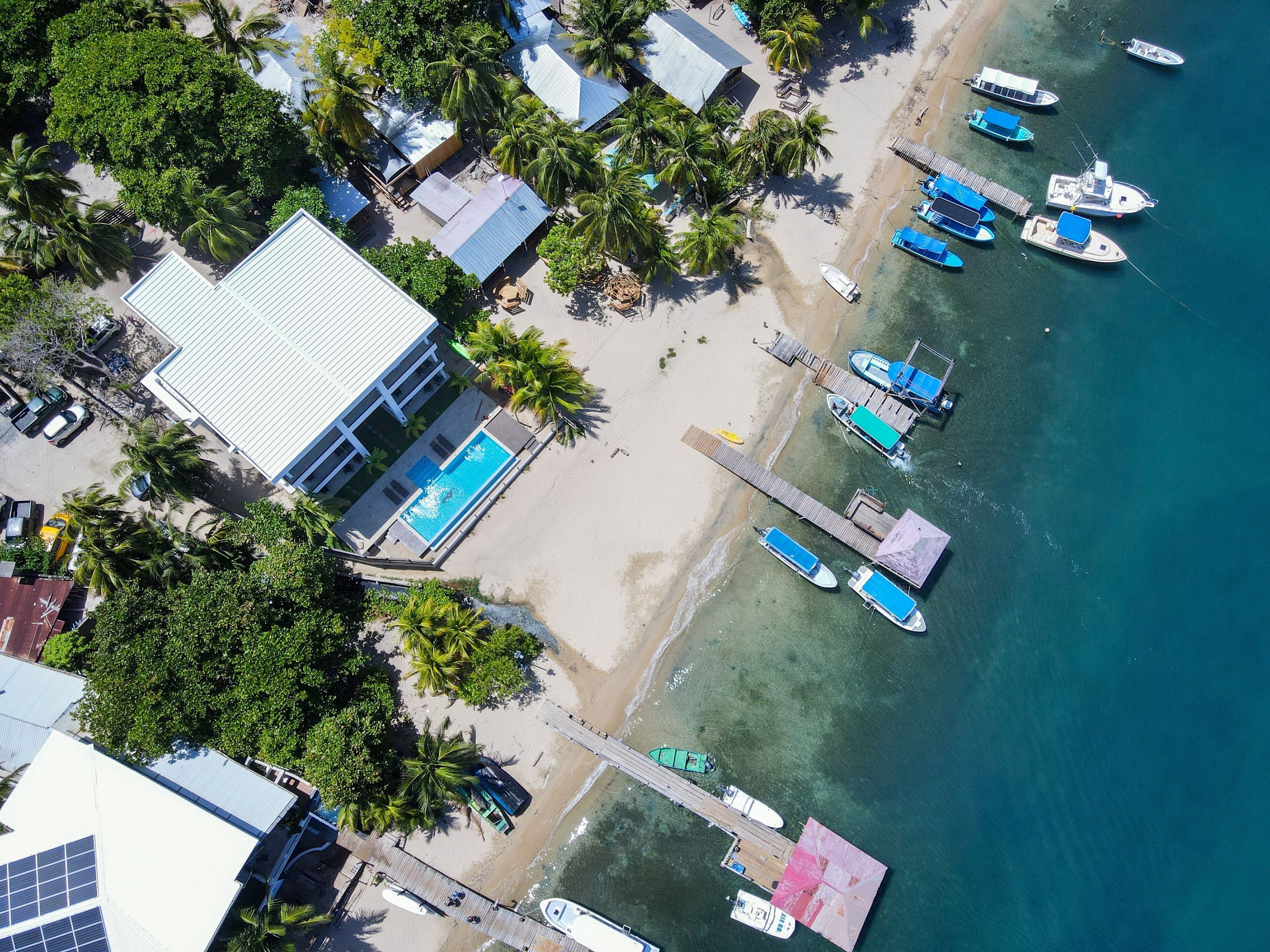 Vue aérienne d’une propriété située sur la côte, avec une piscine, des bateaux amarrés et une plage.