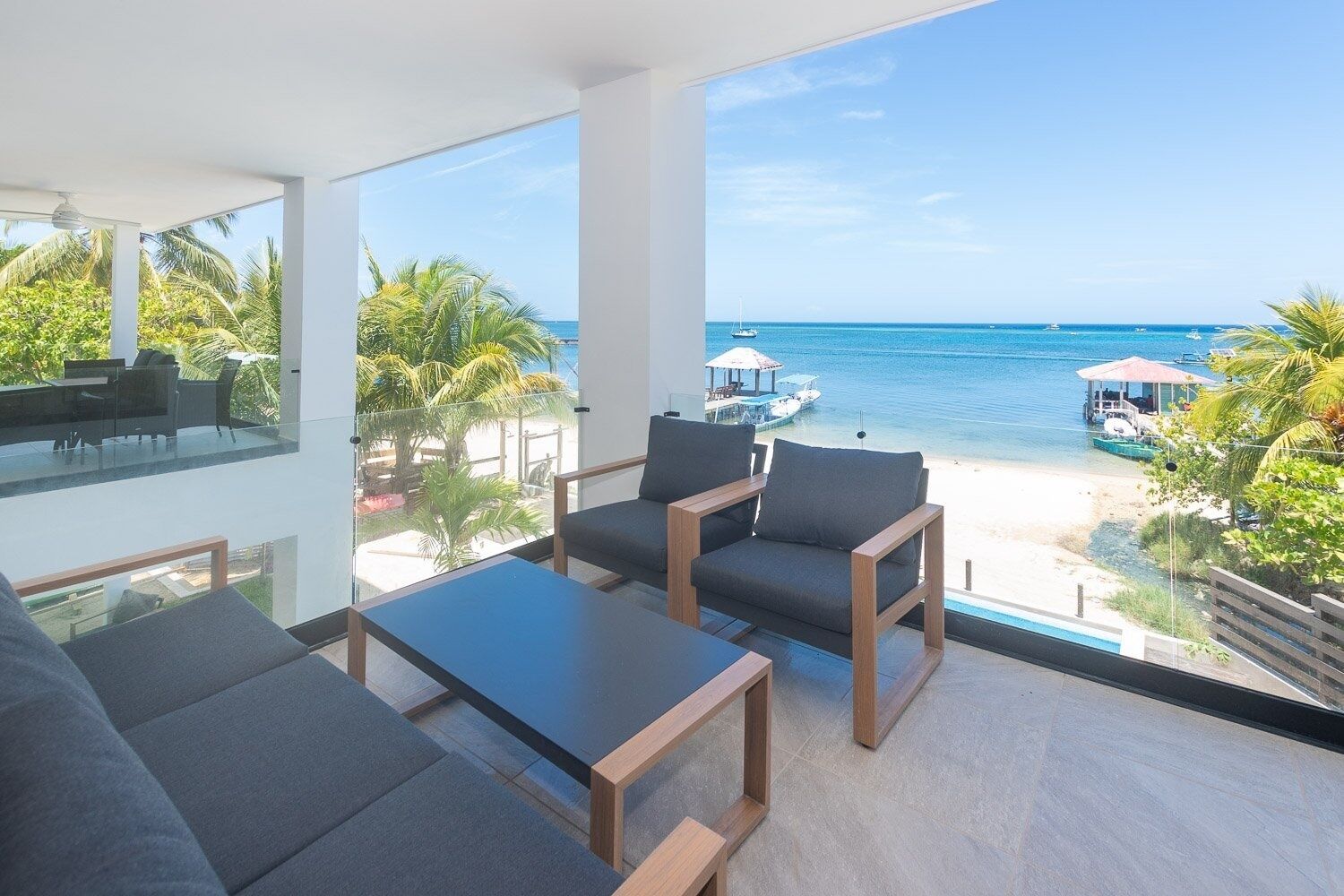 A modern room with a large window overlooking a beach and ocean. There are two grey sofas and a small wooden table.