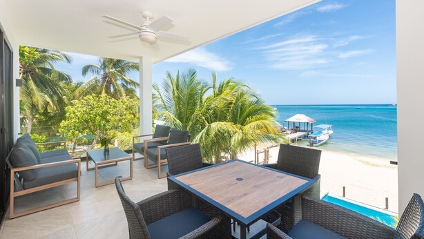 Ein Balkon mit Korbmöbeln, einem Holztisch und Blick auf Strand und Meer.
