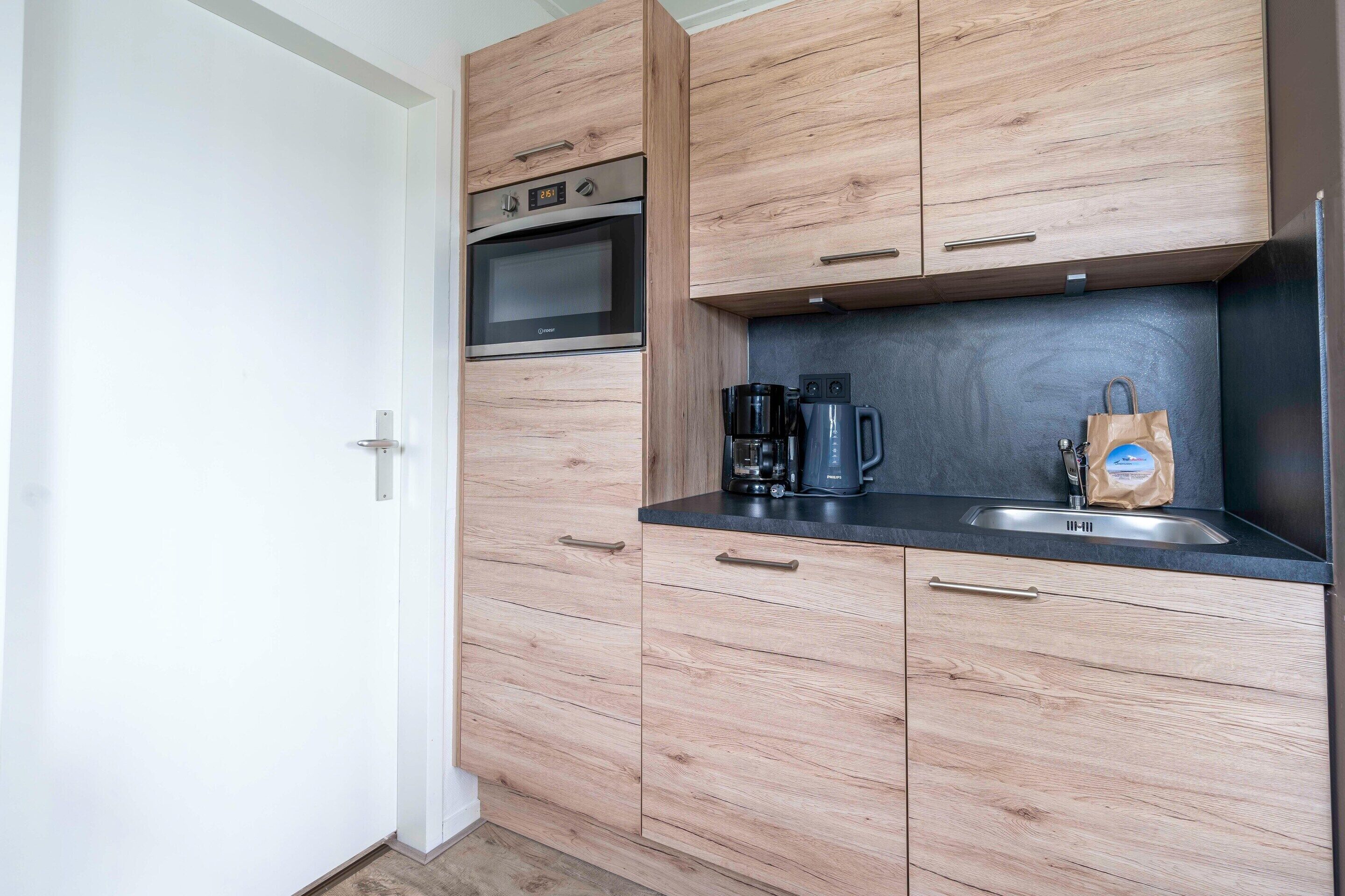 A modern kitchen with wooden cabinets, a built-in oven, a coffee maker, and a sink.