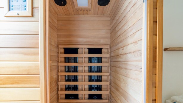Un sauna avec des murs et des bancs en bois, un panneau de commande et une bouche d’aération au plafond.