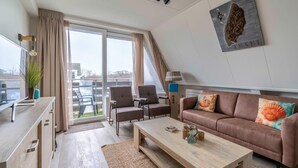 Un salon moderne avec un canapé, des fauteuils, une table basse et une grande fenêtre agrémentée de rideaux.