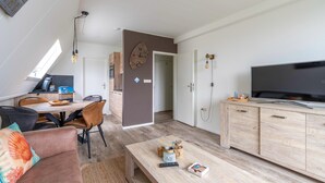 Un salon moderne comprenant un canapé, une table basse, un téléviseur et un coin repas avec des chaises et une table.