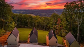A row of modern, single-story houses with sloped roofs, set against a backdrop of a forest and a river, during sunset. - Rally House Pickleball Cabin by Red White & Blue Views (Lookout Mountain)