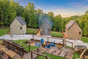 A rustic cabin area with three cabins, a fire pit, and a wooden deck. - Match Point | Pickleball Cabin by Red White & Blue Views (Lookout Mountain Georgia)