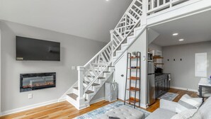 Een moderne woonkamer met een trap, een open haard, een televisie en een keukenhoek.