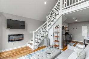 A modern living room with a staircase, a fireplace, a television, and a kitchen area. - Red White and Blue Views| 4 Cabins + 2 Courts (Lookout Mountain)