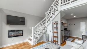 Un salon moderne avec un escalier, une cheminée, un téléviseur et un coin cuisine.