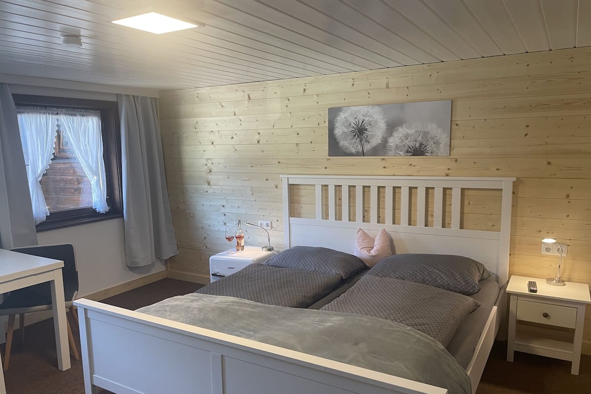 Une chambre à coucher comprenant un lit, des tables de chevet, une commode, un bureau et une fenêtre avec des rideaux.