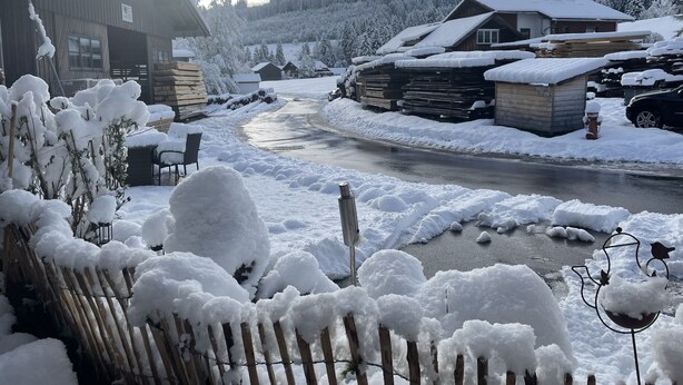 Paesaggio rurale innevato con case di legno, un fiume e una recinzione in legno.
