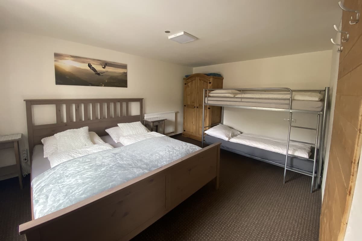 Une chambre d’hôtel avec un lit en bois, un lit superposé, une armoire en bois et un tableau au mur.