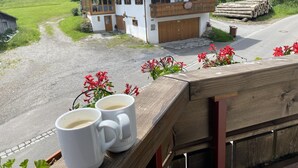 Un chalet con un balcone in legno, un vialetto sterrato e vista su una valle verde.