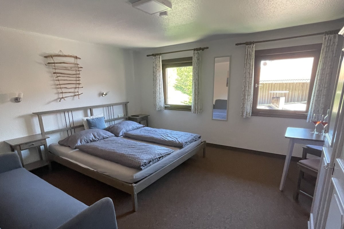 Une pièce comprenant un lit, un bureau, une chaise et une fenêtre avec des rideaux.