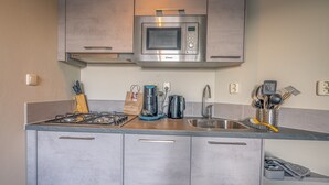 A kitchen with a built-in microwave, gas stove, sink, and various utensils. - Tasteful 2-person Apartment Near the Center of De Koog (De Koog)