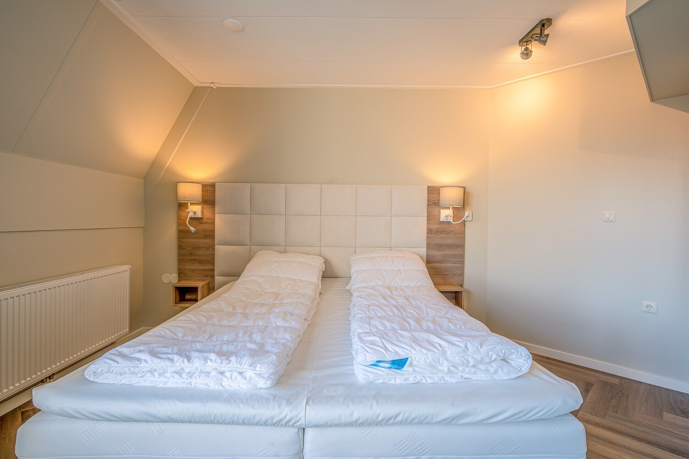 Un lit simple avec une tête de lit en bois, deux lampes de chevet et un radiateur blanc.