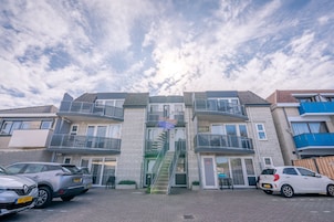 A multi-story residential building with a central staircase, balconies, and a parking area with cars.