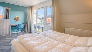 A hotel room with a bed, a desk, a chair, a window, and a view of the outside. - Tasteful 2-person Apartment Near the Center of De Koog (De Koog)