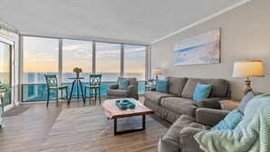 Uma sala de estar ampla com uma grande janela com vista para o mar, um conjunto de sofás aconchegante e uma mesa de centro de madeira.