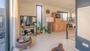 A modern living room with a TV, a wooden cabinet, and a dining area with a table and chairs. - Charming 2-person Holiday Home on the Brink in De Koog (De Koog)