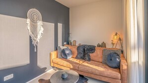 A modern living room with a brown leather sofa, decorative pillows, a dreamcatcher, and a lamp. - Charming 2-person Holiday Home on the Brink in De Koog (De Koog)