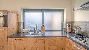 A modern kitchen with wooden cabinets, a stainless steel sink, a kettle, and a gas stove. - Charming 2-person Holiday Home on the Brink in De Koog (De Koog)