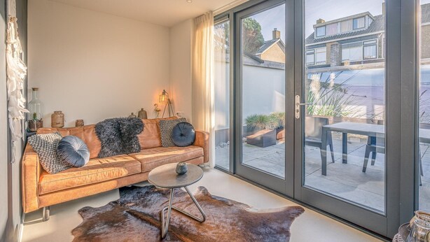 A modern living room with a leather sofa, a glass door leading to an outdoor patio, and a cowhide rug. - Charming 2-person Holiday Home on the Brink in De Koog (De Koog)