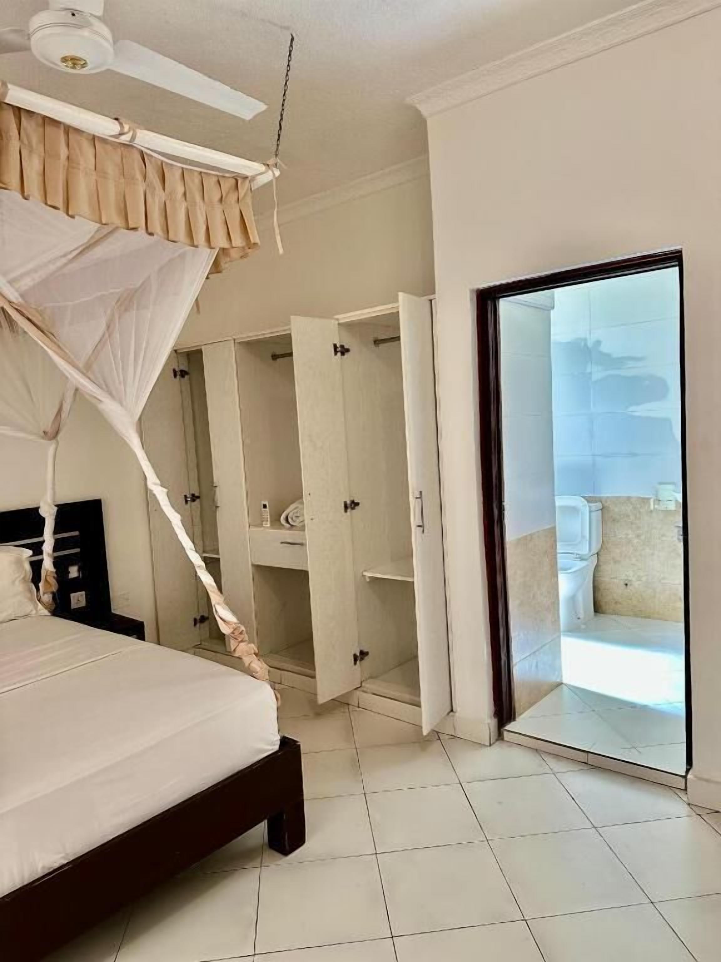 Un dormitorio con cama de dosel, un armario y un baño con inodoro y lavamanos.