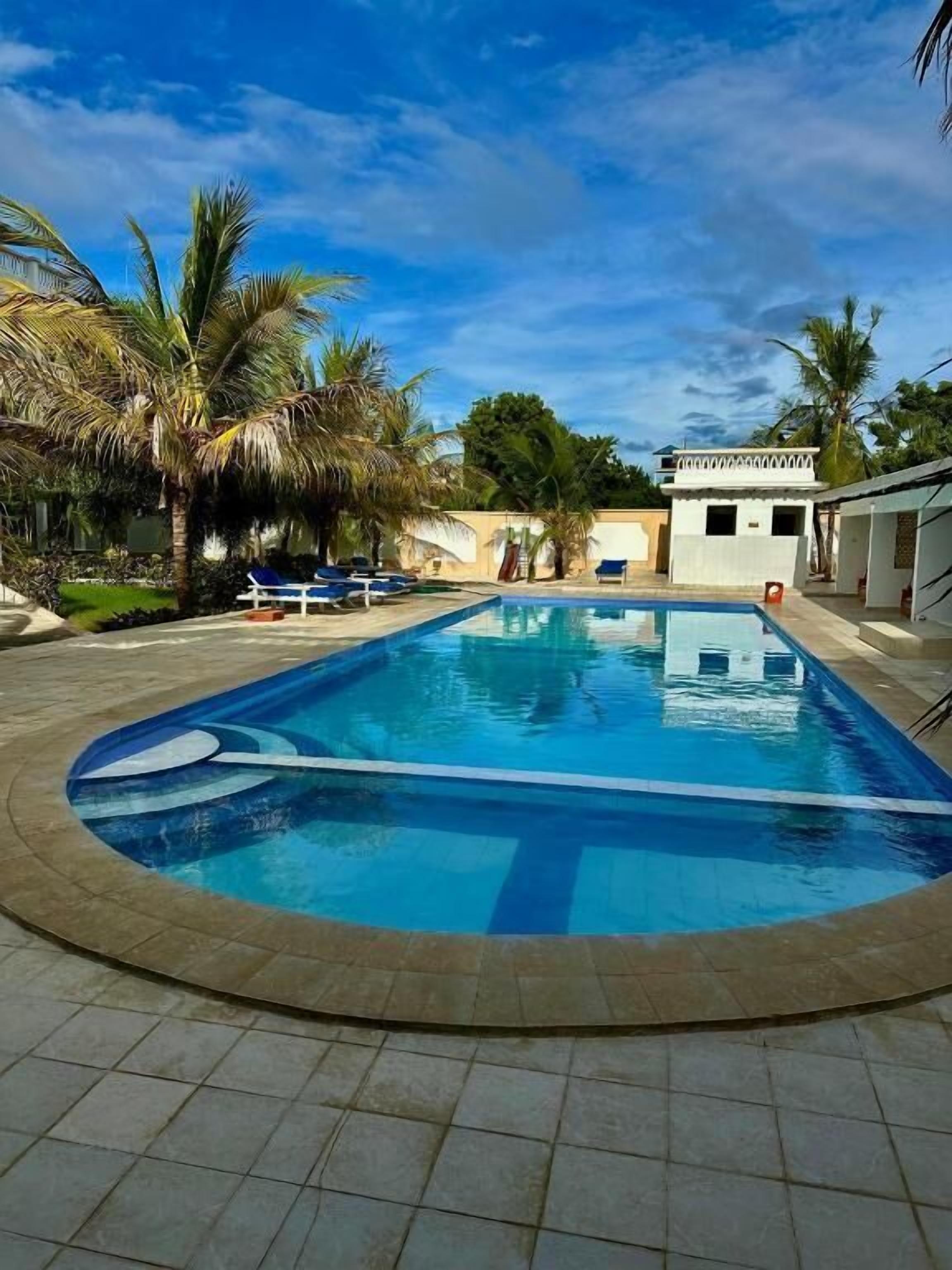 A swimming pool with lounge chairs and palm trees.