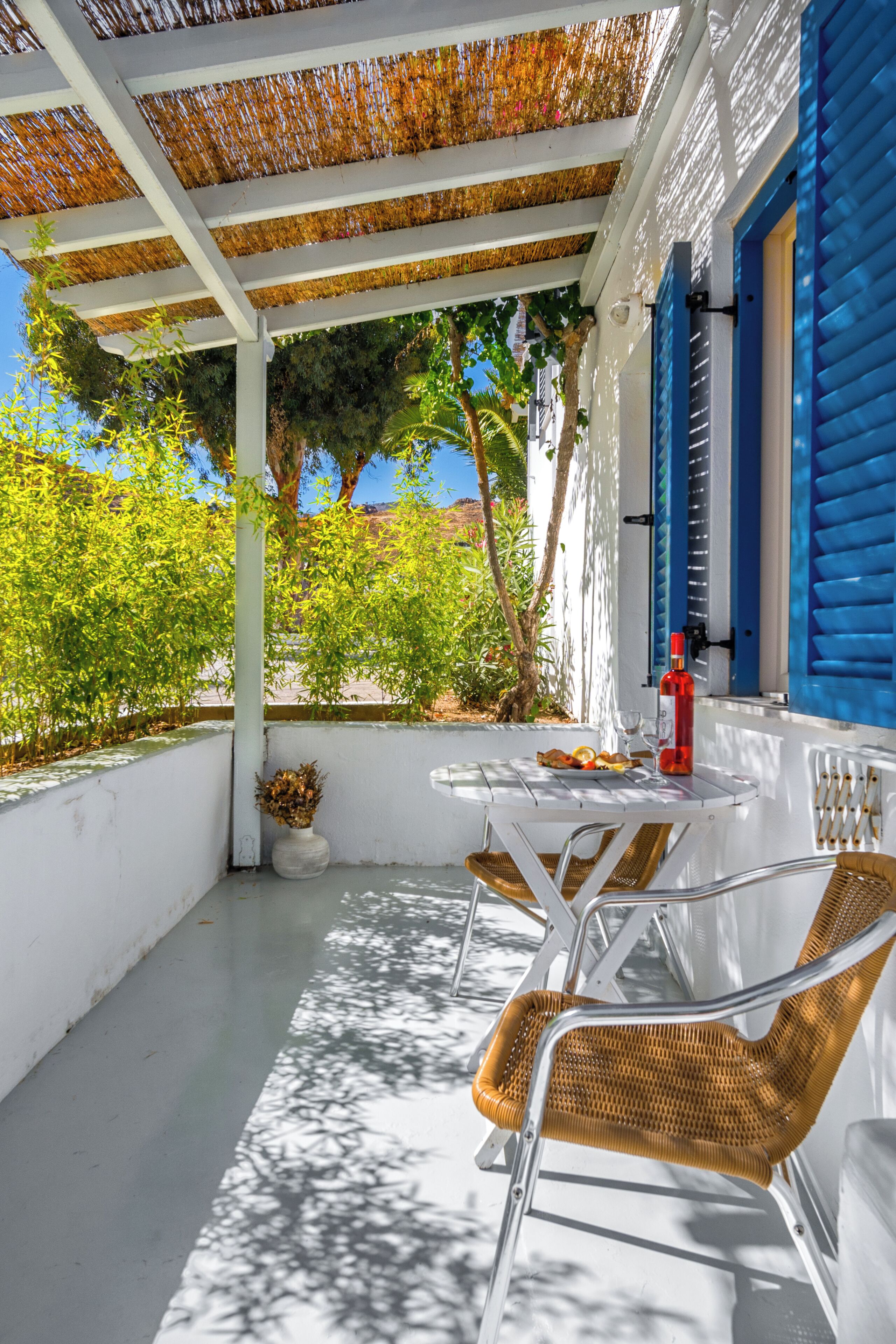 Una zona salotto esterna coperta, con pareti bianche, persiane blu e un tavolo con sedie.