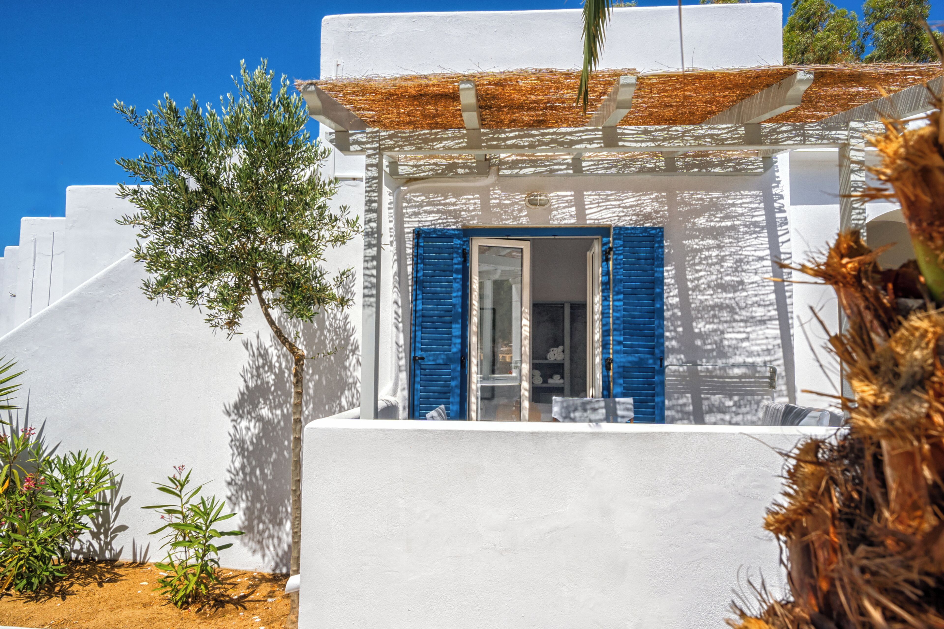 Un edificio blanco con contraventanas azules, cielo despejado y algo de vegetación.