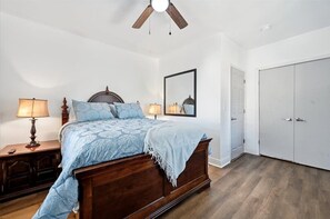 A bedroom with a wooden bed, two bedside lamps, a ceiling fan, a large mirror, and a wardrobe. - Clifton House: 4BR Group Stay PHL + Stadiums + Parking (Sharon Hill)