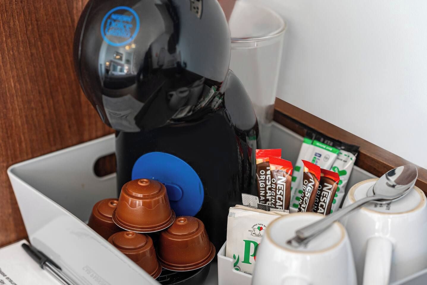 Une machine à café, une tasse, une cuillère et des dosettes de café sur une table.