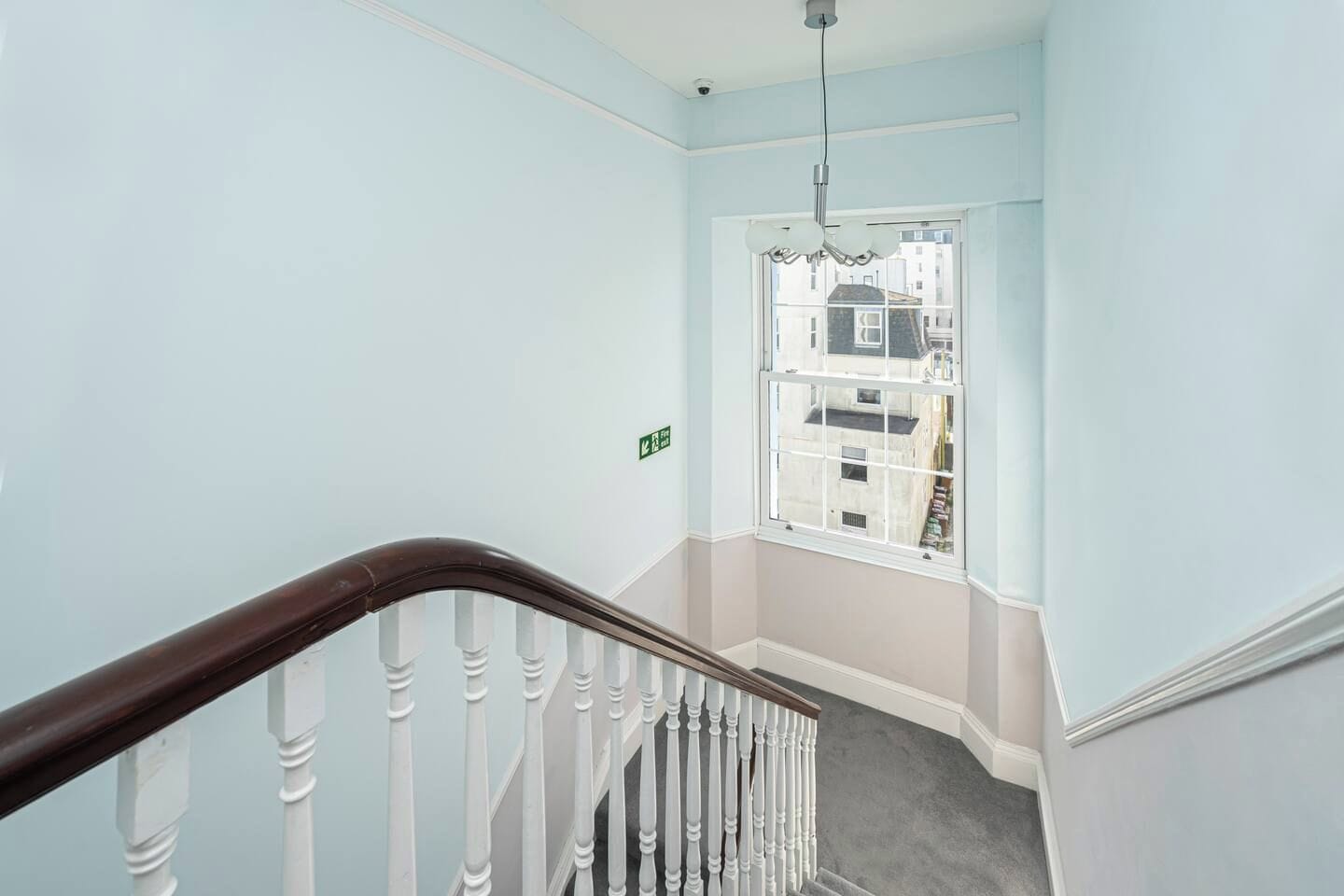 Un escalier doté d’une main courante en bois et de balustrades blanches, menant à un palier d’où l’on peut admirer la vue sur les b âtiments environnants.