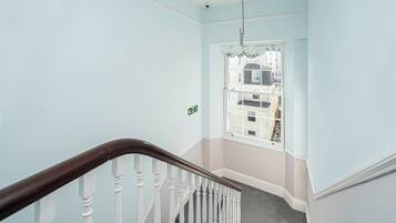 A staircase with a wooden handrail and white balusters, leading to a landing with a view of buildings outside.