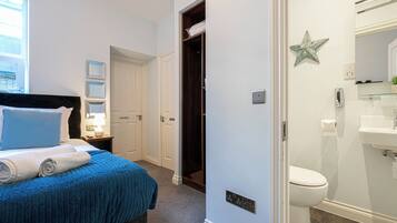 A bedroom with a bed, a nightstand, a window, and a bathroom with a toilet and sink.