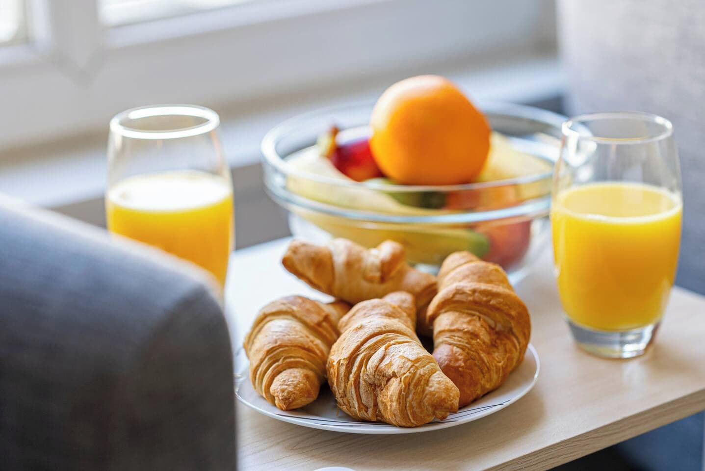A breakfast setting with croissants, fruit, and orange juice on a tray.