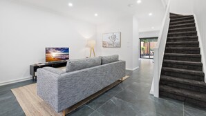 Ein modernes Wohnzimmer mit grauem Sofa, Flachbildfernseher, Lampe und einer Treppe.
