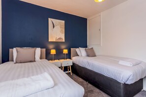 Une chambre d’hôtel avec deux lits, une table de chevet avec des lampes, un tableau au mur et une fenêtre.