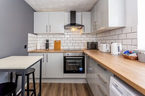 Cuina compacta amb armaris blancs, forn negre, torradora i taula de tall de fusta.