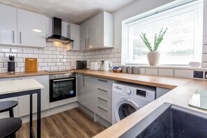 Une cuisine compacte avec des meubles blancs, un four à micro-ondes, un grille-pain et un lave-linge encastré.
