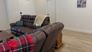 A living room with a brown leather sofa, a plaid blanket, and a painting on the wall. - Beautiful brand new home. Just entered VRBO market November 6.  All things new! (Lubbock)